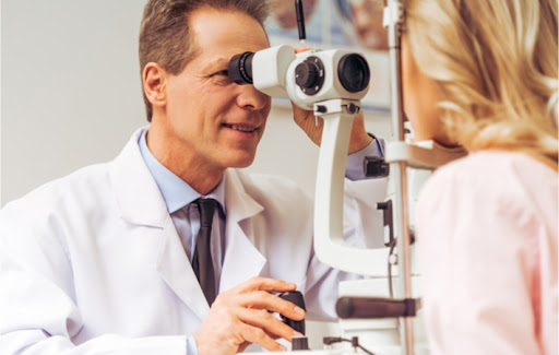 Professional middle aged male optometrist looks like a slit lamp while examining the eyes of a blonde female patient.